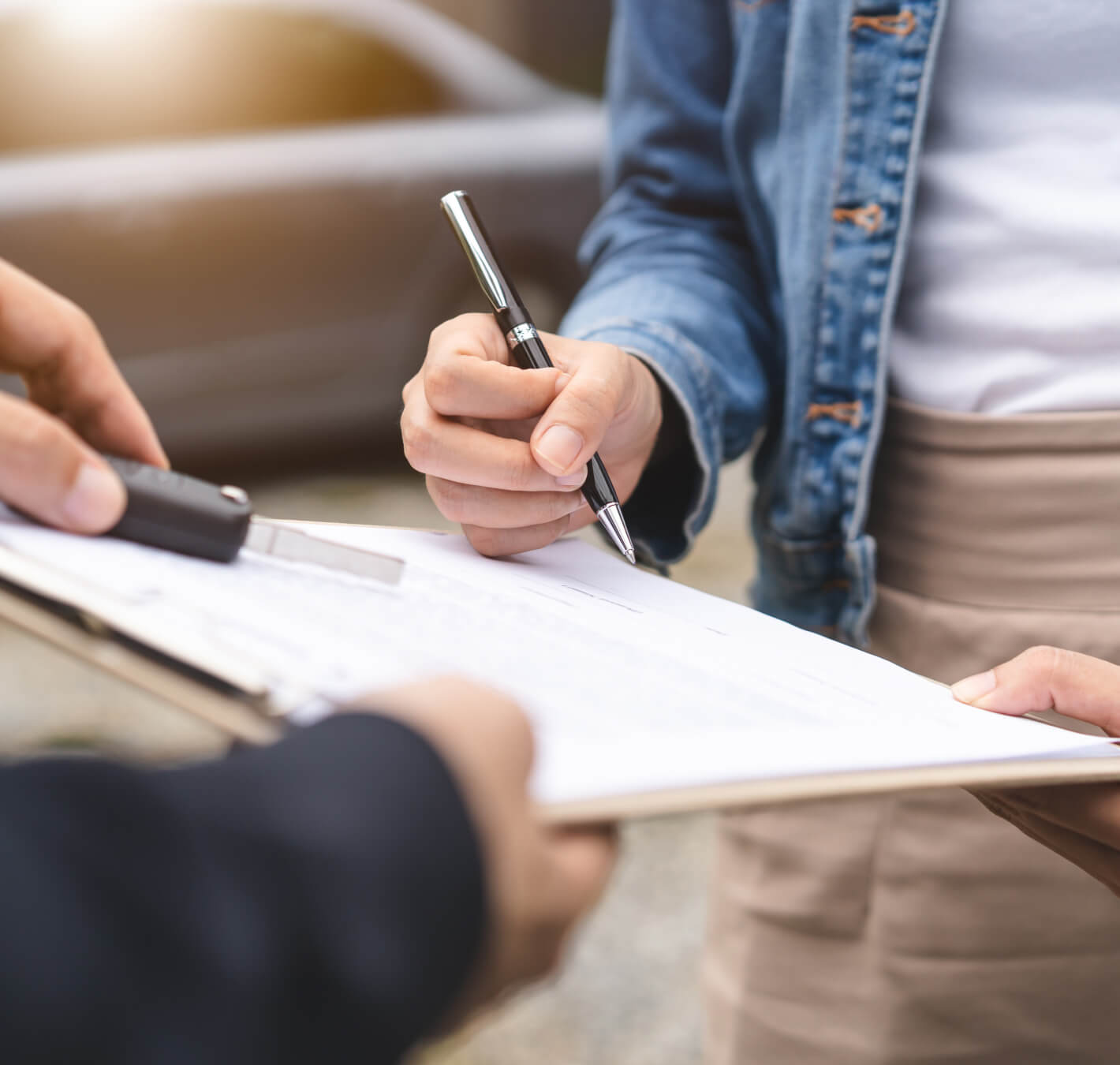 Close-up of a customer signing paperwork on a clipboard to receive a car key.