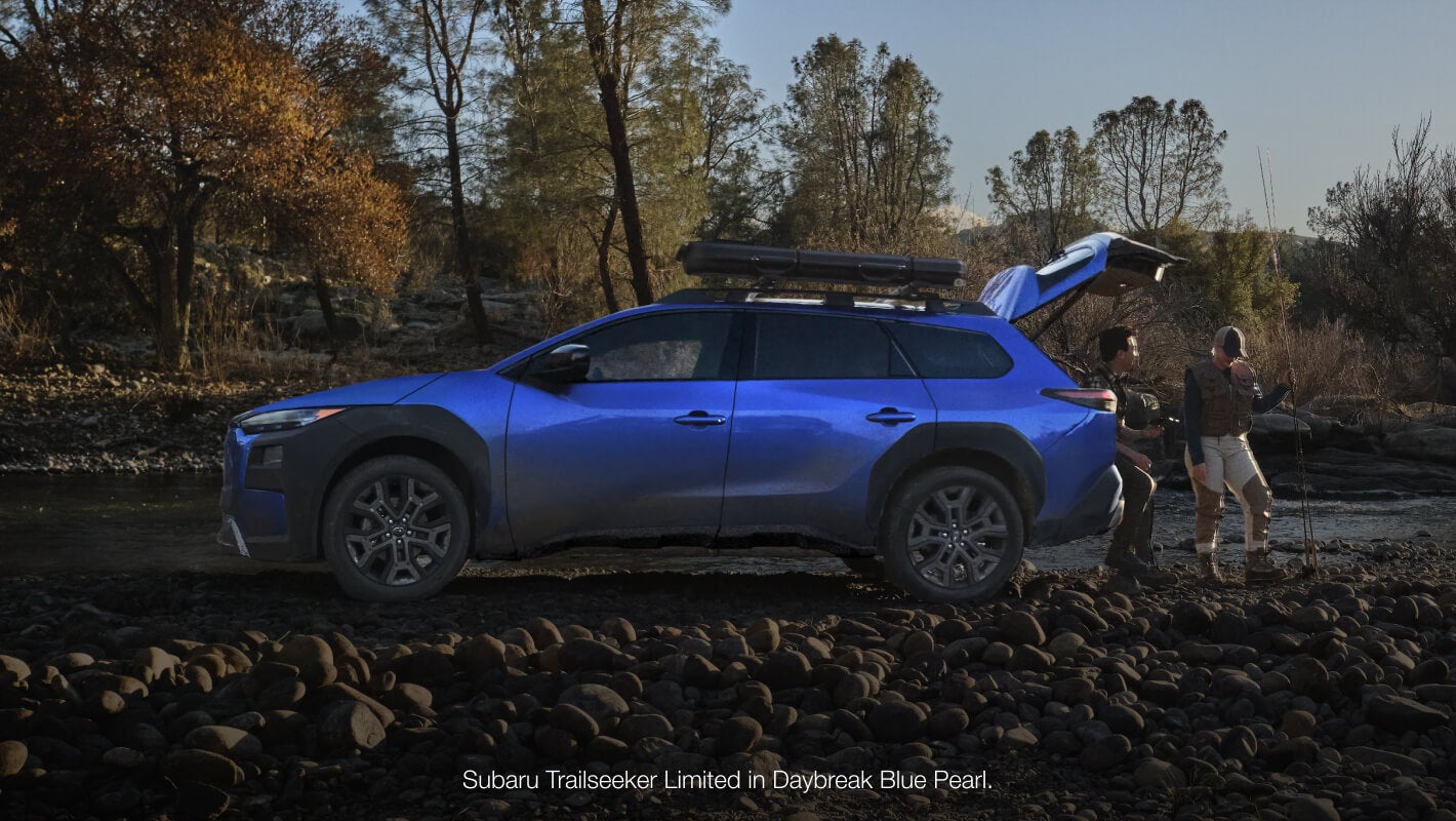 Profile view of the Subaru Trailseeker Limited in Daybreak Blue Pearl parked by a rocky stream.