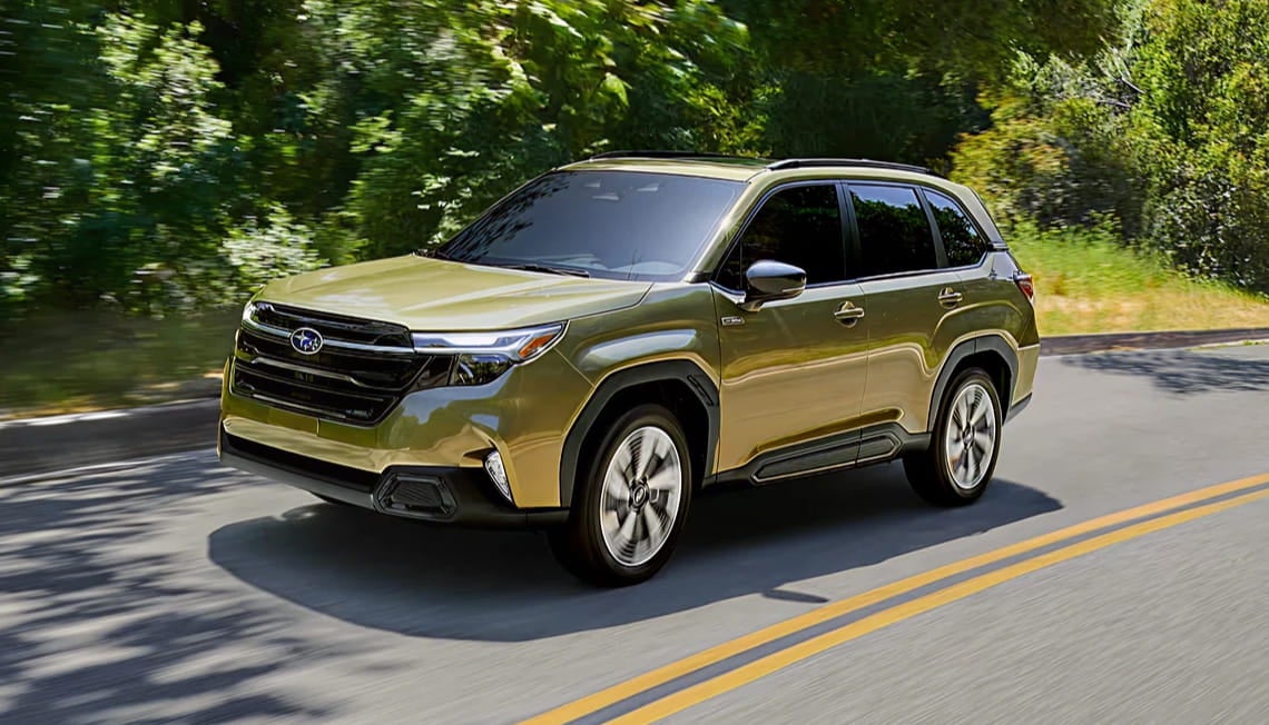 A 2026 Subaru Forester Hybrid drives on a sunny, tree-lined road. The vehicle has a sleek, modern design, conveying a sense of adventure and elegance.