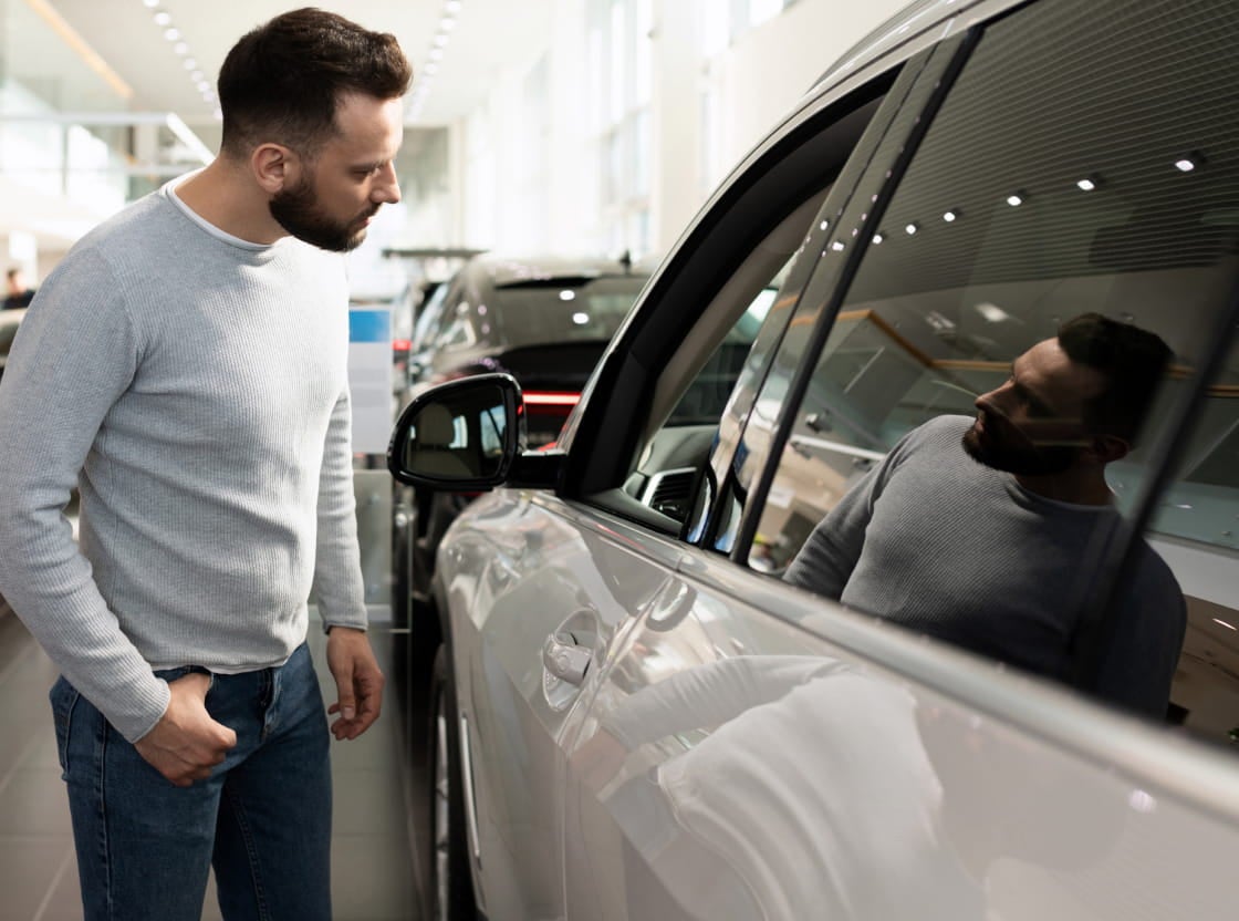 Man inspecting a white vehicle inside a car dealership showroom.